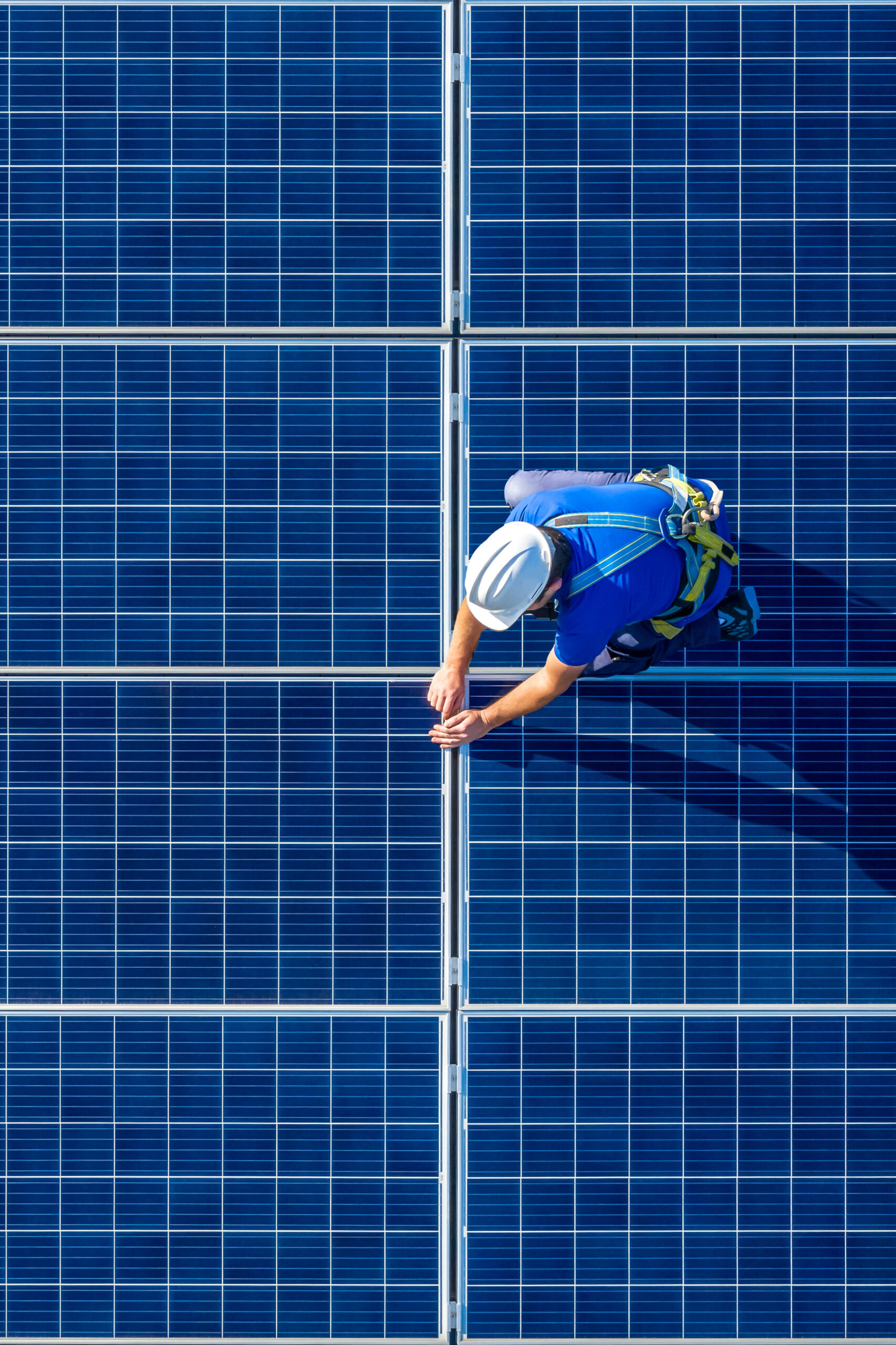 Male engineer in blue suit and protective helmet installing photovoltaic panel system. Professional electrician mounting solar module on roof. Alternative energy ecological concept